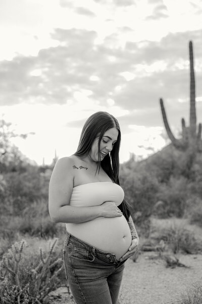 Black and white image of mother looking down at her belly against desert backdrop.