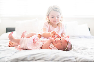 Big sister and newborn sister wearing pink sitting on a bed