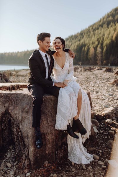 Bride and groom sitting on tree stump in the Pacific Northwest, laughing out loud as the groom has his arm around the bride.
