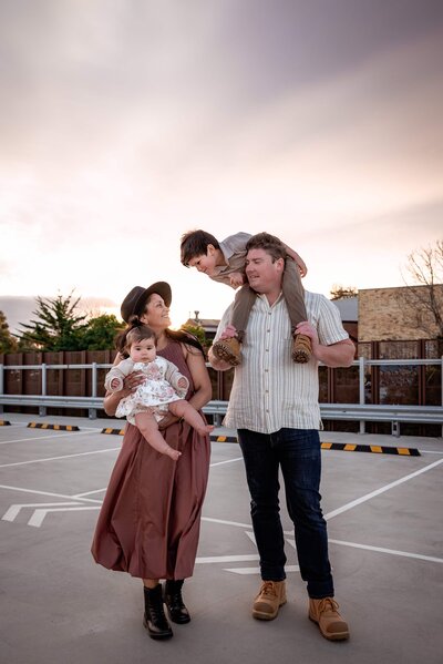 Family of four with a son and baby daughter taken at dusk in a roof top carpark