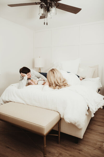 Family of four in a timeless off-white colored bedroom lying on the bed.