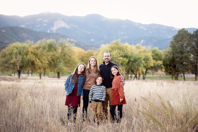 A happy family smiles while standing with each other in a field of tall grass at sunset