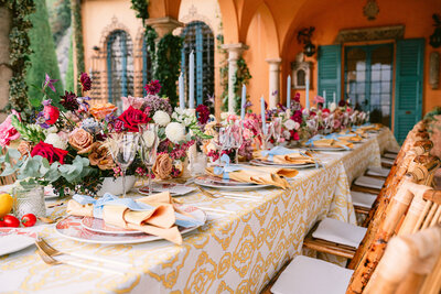 A colorful wedding reception table decorated with bright florals and peach napkins in the courtyard of an luxury hotel in Lake Como