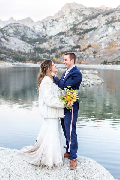 A groom sweetly touches his brides face in front of a beautiful lake view on their mammoth wedding day. 