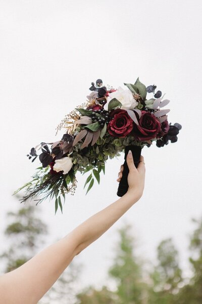 A red and green bouquet held up against a sky.