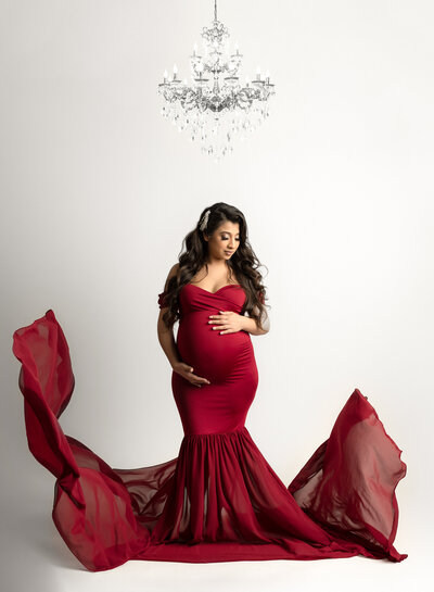 pregnant woman standing under a chandelier wearing a fitted red maternity dress