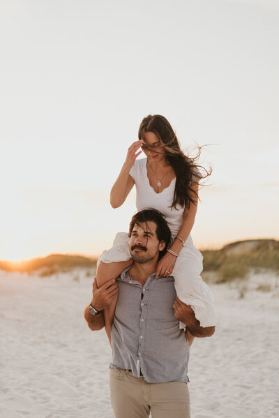 a woman sitting on the shoulder of her husband while looking down at him at Grayton Beach, Florida. 