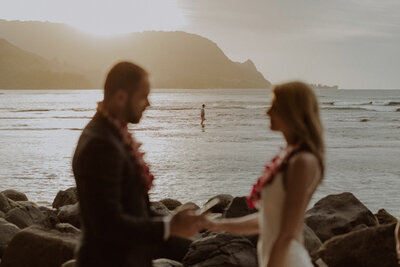 Couple elopes on the beach as a fisherman walks in the water behind them