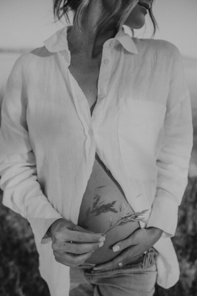 A pregnant mother holds up a bundle of wildflowers to her exposed pregnant belly. 