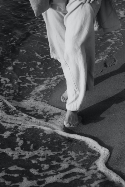 A monochromatic image of bare feet walking along the shoreline, the waves gently lapping over