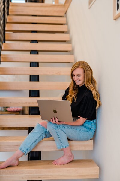 Iowa Brand Photographer and Videographer holds laptop on stairs
