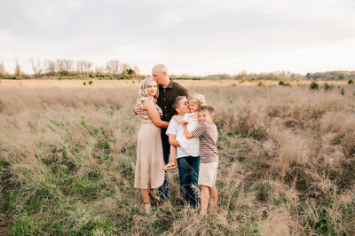 Branson family picture of family cuddling in field at sunset