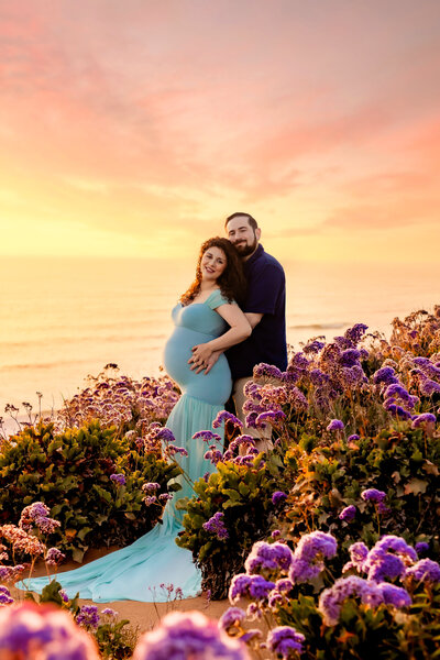 Maternity Photographer, an expectant mother wears a teal dress with her husband amongst purple flowers
