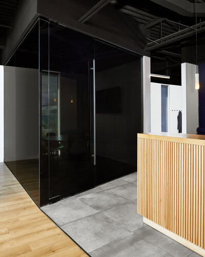 A closed-off meeting room with opaque black glass walls next to a tall wood paneled reception desk