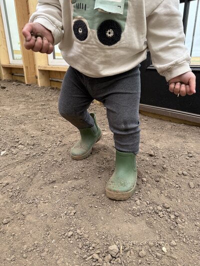 child in green rubber boots walking on dirt during a quiet day on the farm

