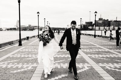 a bride and groom walk down the street in baltimore, laughing