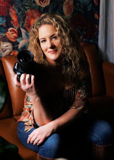 Stefanie Lynn sitting in a brown chair holding her camera posing as a South Shore MA Portrait Photographer