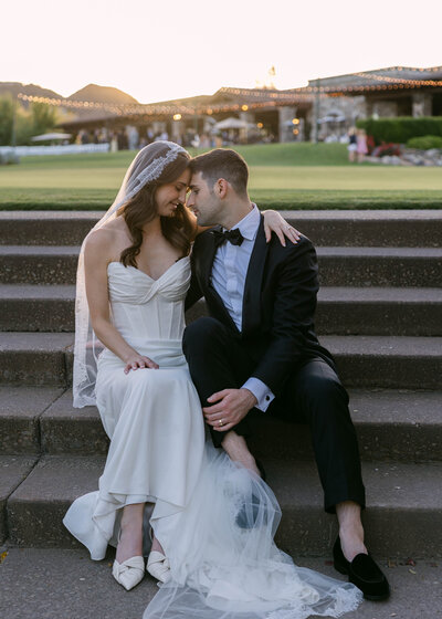 A stunning outdoor wedding ceremony in Scottsdale, Arizona, with a breathtaking mountain backdrop. Guests in vibrant pink dresses watch as the bride and groom exchange vows under a floral arch at sunset.