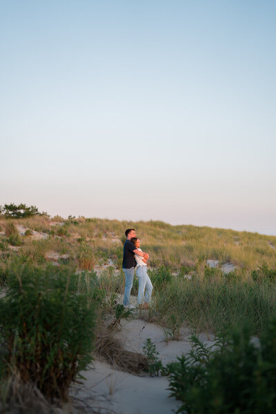 A couple standing in the dunes on the beach at sunset.