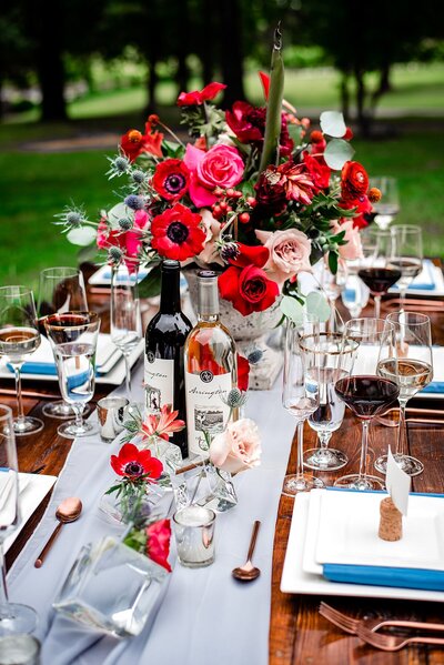 Dark wood farm table with sheer organza table runner and bright red floral centerpieces , white and teal table settings and vineyard themed wedding decor at Arrington Vineyards