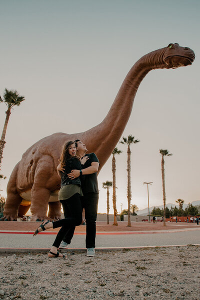 couple embraces in front of dinosaur