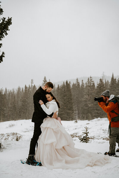 Wedding videographer in beanie captures couple during snowy elopement in Breckenridge.