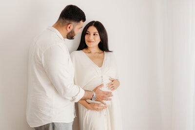 Roshni holding her belly with her husband during her studio maternity photoshoot