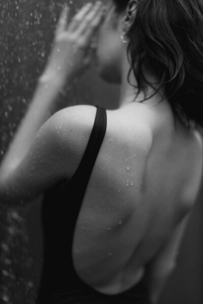 Close-up of a woman in a black swimsuit under a shower, with water droplets glistening on her skin, capturing a moment of elegance and refreshment.