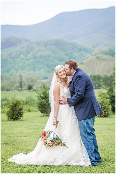 Groom kisses bride in field with mountain views