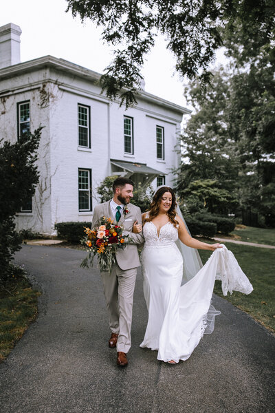 Married couple walking down the road in front of a historic house.