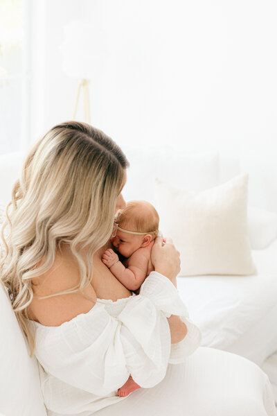 New mom cuddles newborn baby on the couch during in home photo session in Florida