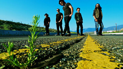 Band portrait of The Mattinee standing on road  weed growing through cracked asphalt in foreground five band members standing in background