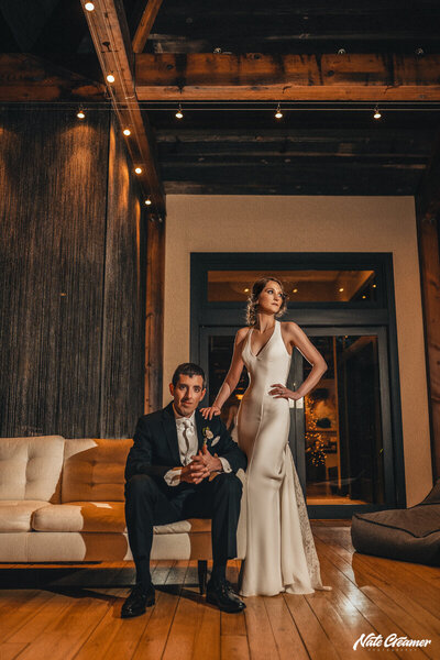 A groom sitting on a sofa while his bride stands next to him at Winvian Farms in Morris, Ct.