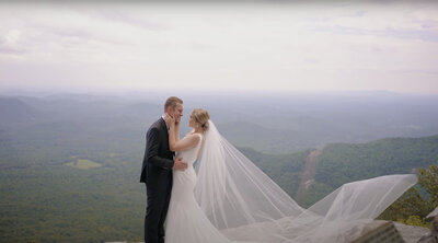 Bride and groom smile at each  other on a mountaintop