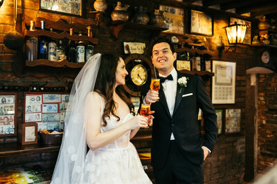 Bride and groom cheer with spritz in a cozy Osteria, blending joy and tradition in the heart of Venice