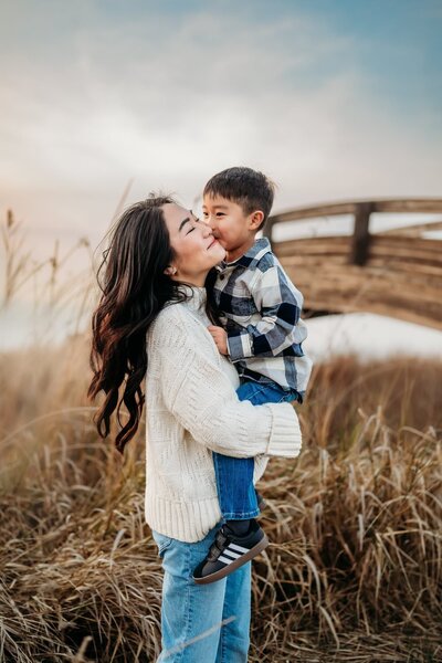 mom holding her son as he kisses her cheek. the sun is setting behind them