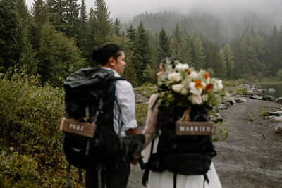 Backpacking couple stand hand in hand with their "just married" sign attached to their backpacks.