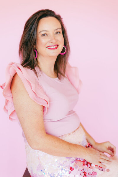 Headshot of Kristin Perrine in a pink dress in front of a pink background