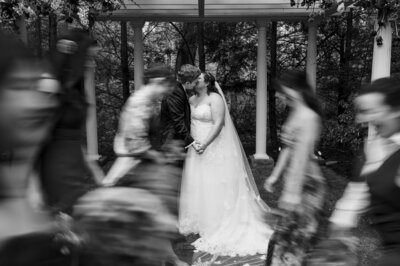 Brides kissing while wedding party passes by in a blur