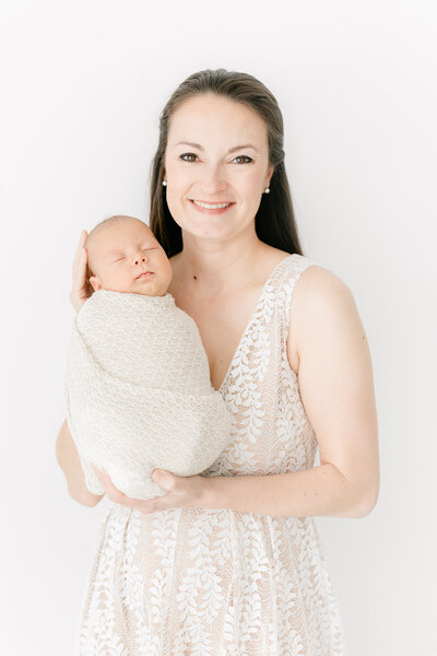 A mother holding her newborn baby up to her face and smiling at the camera by Family Photographer DC
