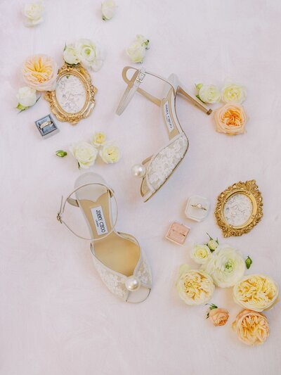 Elegant bridal details styled by a Central Coast wedding planner, featuring lace Jimmy Choo heels, vintage gold frames, floral accents, and heirloom rings.