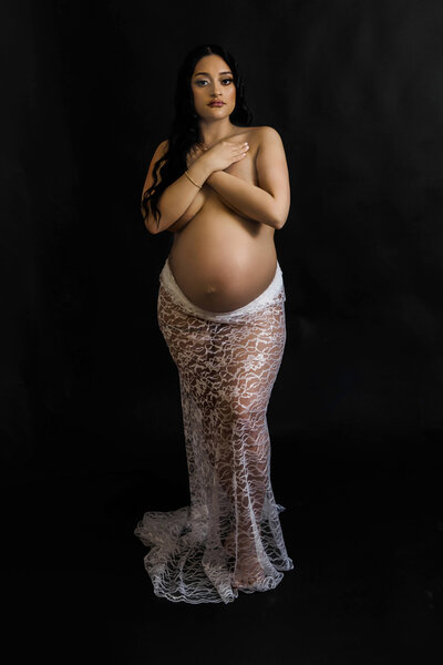Elegant studio maternity portrait in white lace gown on black background