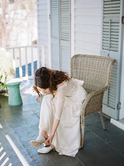 Bride putting on her shoes in a lace and beaded wedding dress with a romantic V-back
