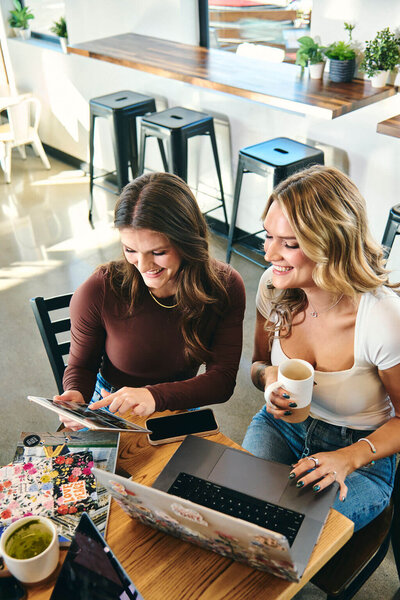 two girls sitting at a table, holding and ipad and pointing at something on it