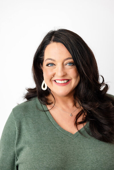 Woman with black hair and a green sweater look directly at camera for her headshot session.
