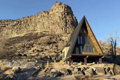 The nearly completed Perrine Hideaway A-frame cabin, featuring a black metal roof, large glass windows, and a rugged canyon backdrop