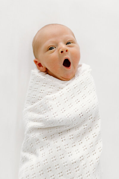 Baby wrapped in white swaddle yawning during newborn photos with Indianapolis newborn and family photographer Capturing Simplicity Photography