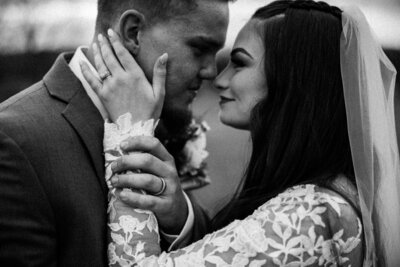 black and white photo of a bride and groom leaning in for a kiss while the bride cups her grooms cheek