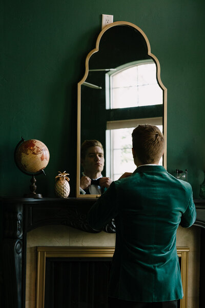 Groom looks into gold mirror to adjust his bowtie before the wedding ceremony.
