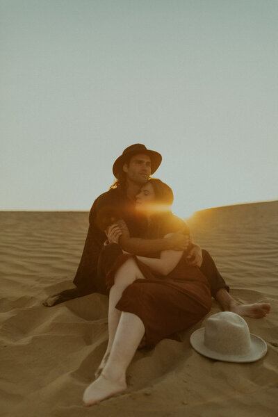 couple sitting in sand dunes and embracing